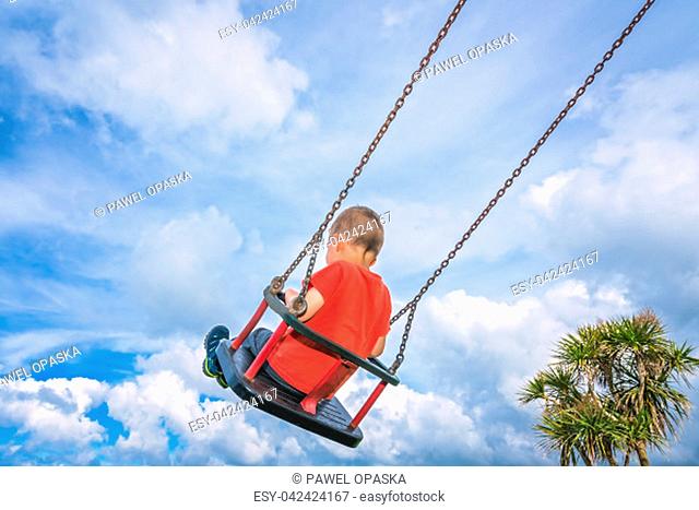 Little caucasian boy having fun on a sling om a playground