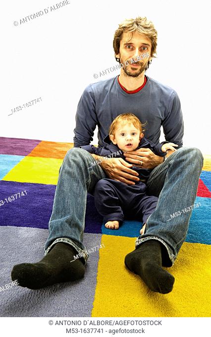 Father hold his 10 months old baby while on a multi coloured carpet