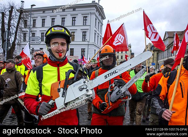 28 November 2023, Mecklenburg-Western Pomerania, Schwerin: Forestry workers with chainsaws take part in a protest action in the ongoing wage dispute in the...