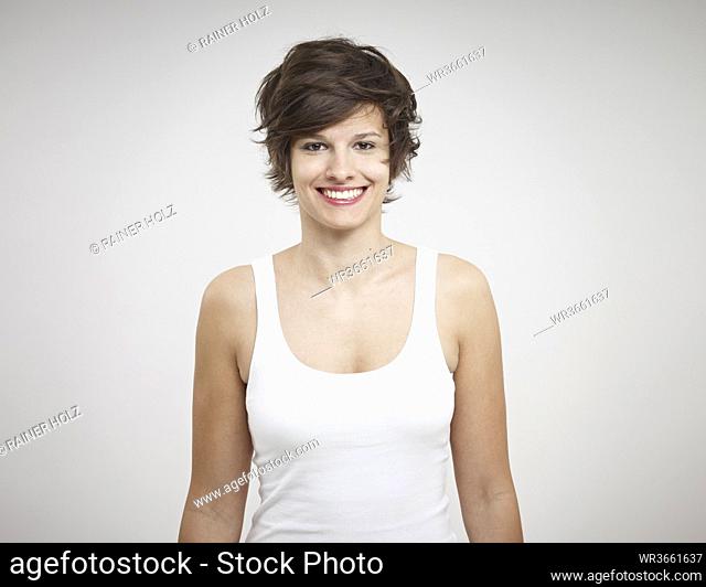 Portrait of young woman standing against white background, smiling