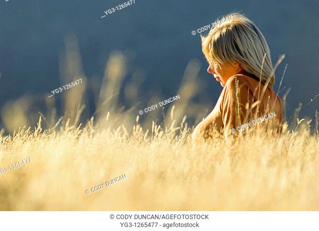 Blond female sitting in golden autumn grass in Arthur's Pass, New Zealand