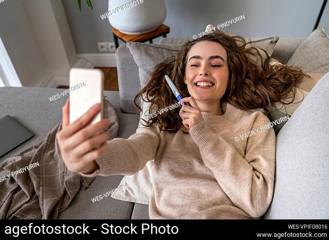 Happy young woman showing pregnancy testing kit on video call at home