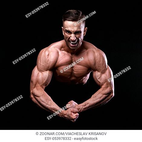 Scream of rage in the bodybuilder during training. Bodybuilding, fitness model. Emotions. On black background
