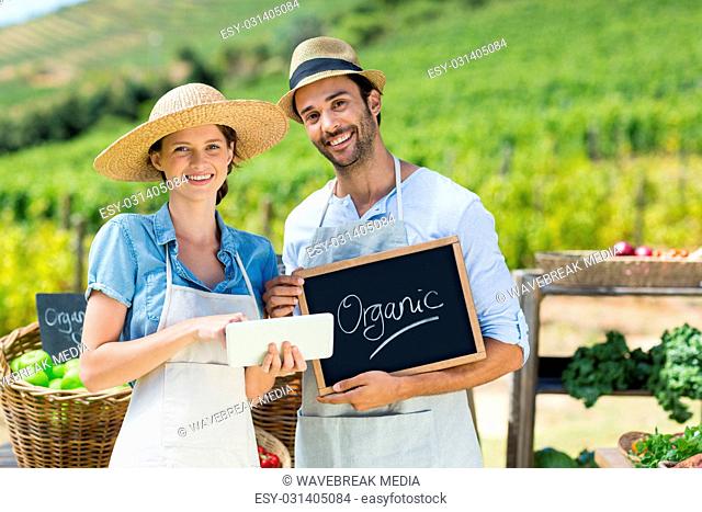 Portrait of happy couple holding chalkboard while using digital tablet
