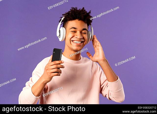 Technology and lifestyle concept. Portrait of carefree attractive young man enjoying fine sound, listening music with headphones look delighted awesome quality...