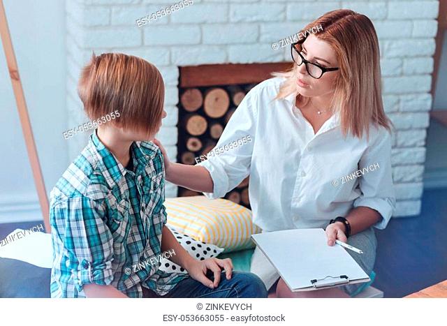 What is your biggest fear. Thoughtful female therapist sitting next to a male youngster and asking him about his worries while he attending a professional...