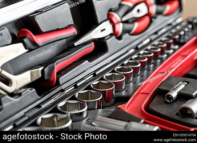 Black-red pliers and a red saw in the dark toolbox. Between them there are different nozzles. Closeup low aperture photo. Horizontal