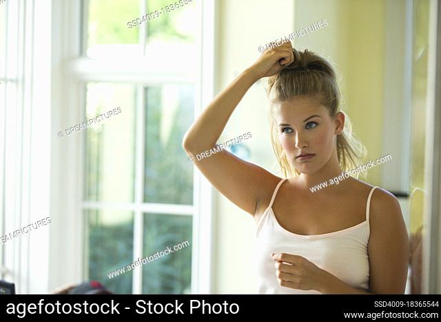 Portrait of young woman in bathroom looking in the mirror while putting her hair up