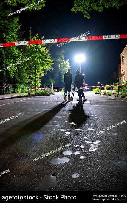 26 August 2023, Hamburg: A light pole illuminates the cordoned-off crime scene while forensic technicians work with a 3D scanner