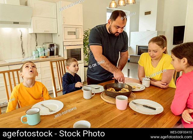 Father serving breakfast to woman and children at home