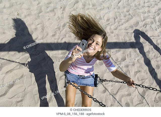 High angle view of a young woman sitting on a swing and holding a mobile phone