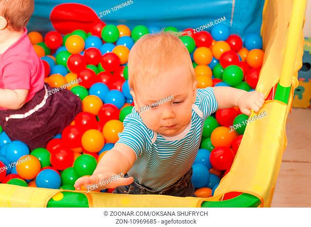 Three babies playing with multicolored small balls inside the playpen