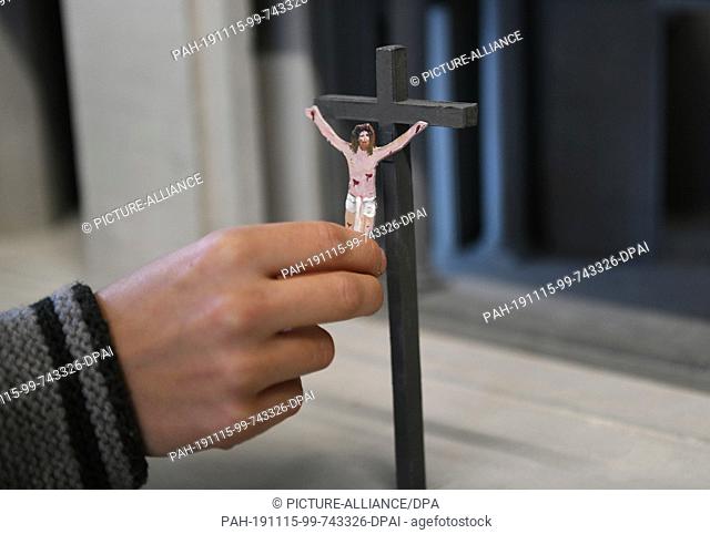 15 November 2019, Bavaria, Oberammergau: An assistant of the stage and costume designer hangs a Jesus figure on a cross in a model of the stage for the Passion...
