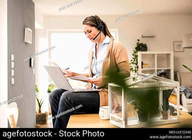 Female professional examining document while sitting with laptop at home