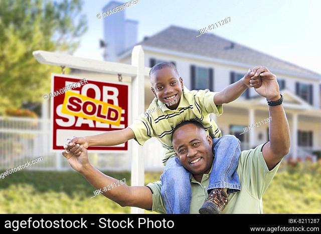 Happy african american father and son in front of home and sold for sale real estate sign