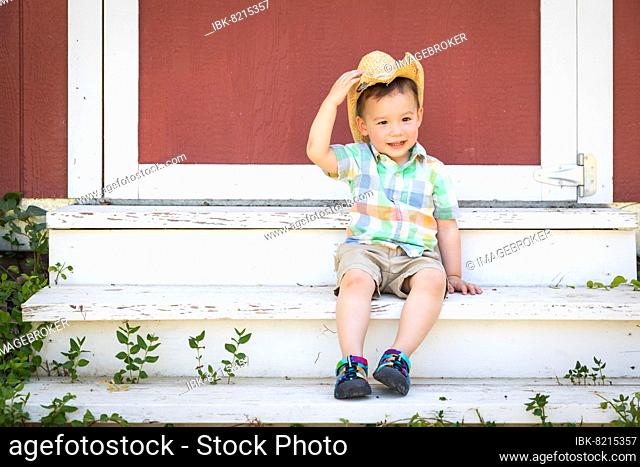 Young mixed-race chinese and caucasian boy wearing cowboy hat relaxing on the steps