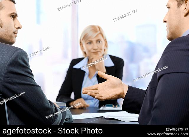 Businesspeople sitting at table in office, discussing work at meeting. Focus on explaining hand