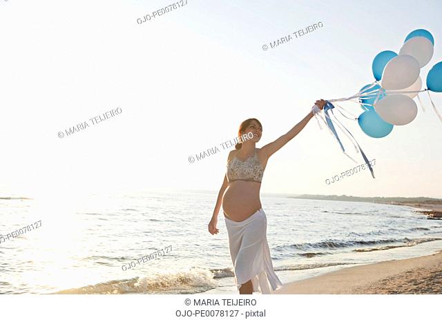 Pregnant woman carrying balloons on beach