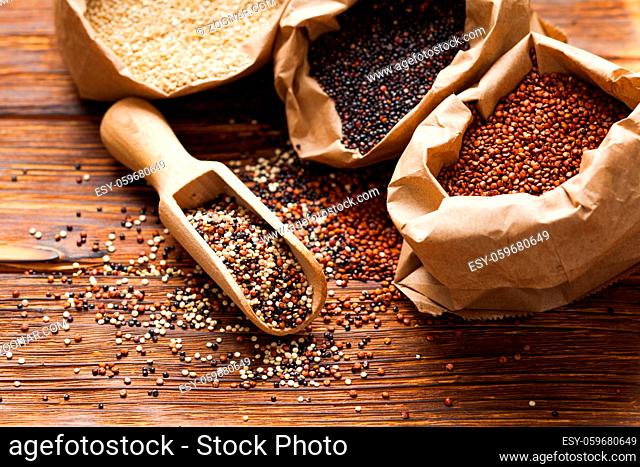 Mix of quinoa seeds in the wooden scoop. White, red and black quinoa in paper bags on the table, healthy lifestyle food concept
