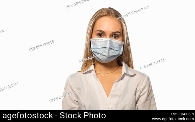 Nurse in a medical mask and white uniform with blond loose hair looking at the camera. Isolated on white background