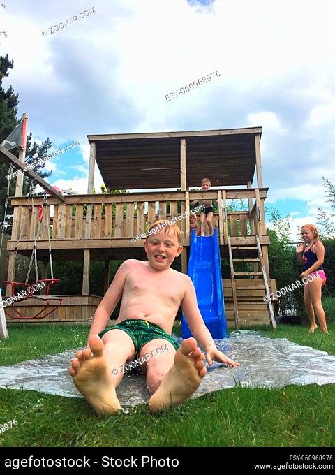 Children playing on a waterslide in the garden during summertime
