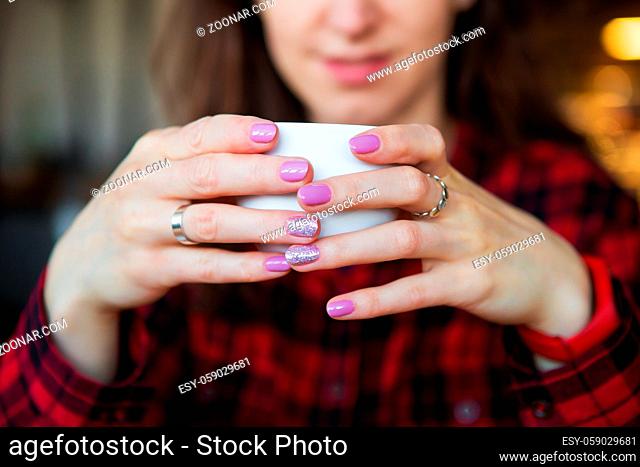 The girl smiles while holding a cup of coffee. Close-up