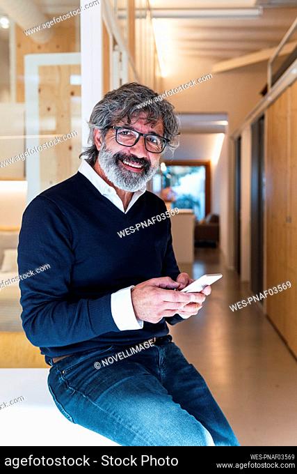Happy senior man wearing eyeglasses sitting with smart phone on table at home