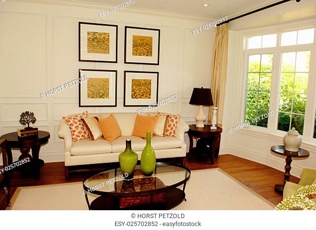 A nice living room with a large window, sofa and chairs with pictures on.the wall and an glass table in a new house.