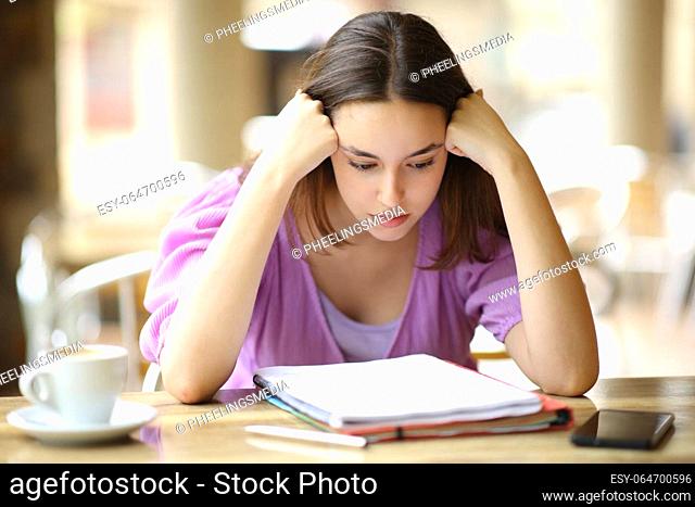Student studying hard reading notes from notebook in a restaurant terrace