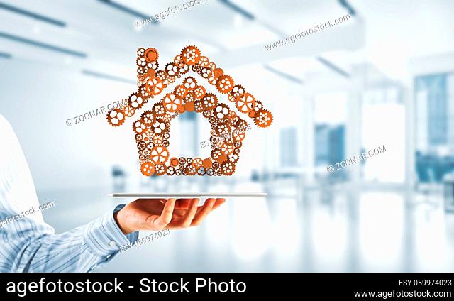 Close of businessman holding tablet pc with house sign made of connected gears. Mixed media