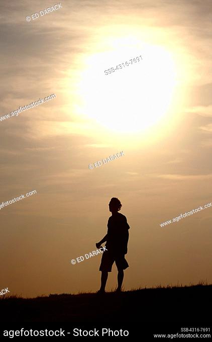 USA, Colorado, Silhouette of man drinking beer on open plains, Setting sun
