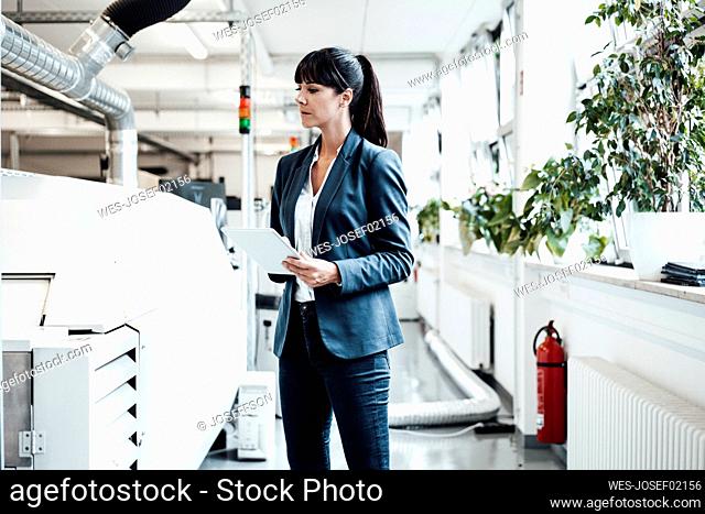 Businesswoman investigating while looking at machinery and holding digital tablet in industry