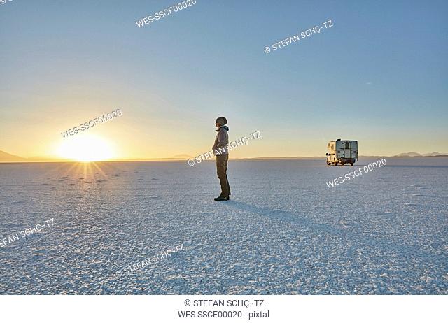 Bolivia, Salar de Uyuni, woman standing at camper on salt lake at sunset