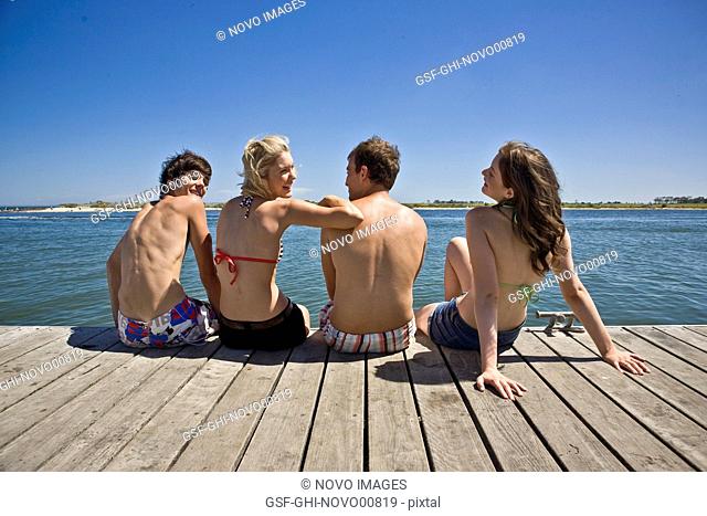 Two Young Couples Sitting on Edge of Pier, Rear View