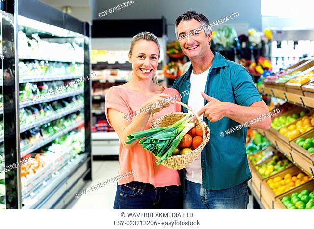 Smiling couple pointing basket with vegetables at the supermarket