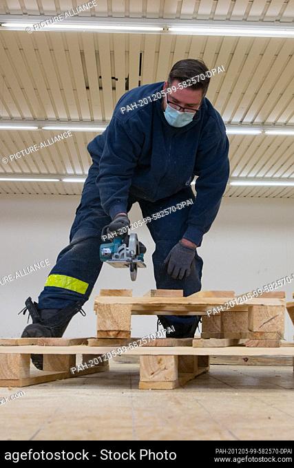 05 December 2020, Wilhelmshaven: A THW worker saws pallets apart while setting up a vaccination centre in an empty supermarket of about 750 square metres