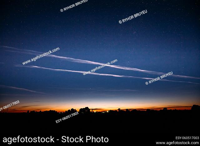 Blue Night Starry Sky And Noctilucent Clouds Above Summer Countryside Landscape. Glowing Stars And Night Shining Clouds. Tenuous Cloud-like Phenomena In The...