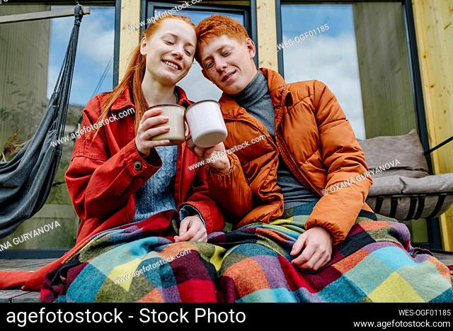 Smiling couple toasting coffee cups sitting on house deck