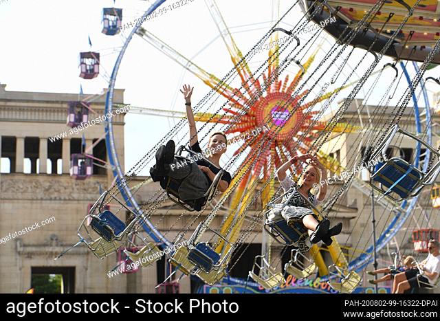 02 August 2020, Bavaria, Munich: The ladies Nina Geyer (l) and Yve Marwan, dressed in traditional costume, are happy to ride in a chain carousel in front of the...
