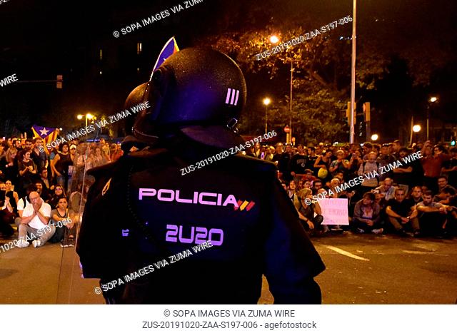 October 20, 2019, Barcelona, Spain: A policeman stands on guard in front of protesters sitting on the ground during the demonstration