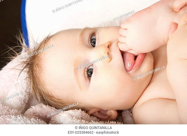 portrait of eight months age blonde lovely cute baby face wet hair licking her foot on mouth lying on towel
