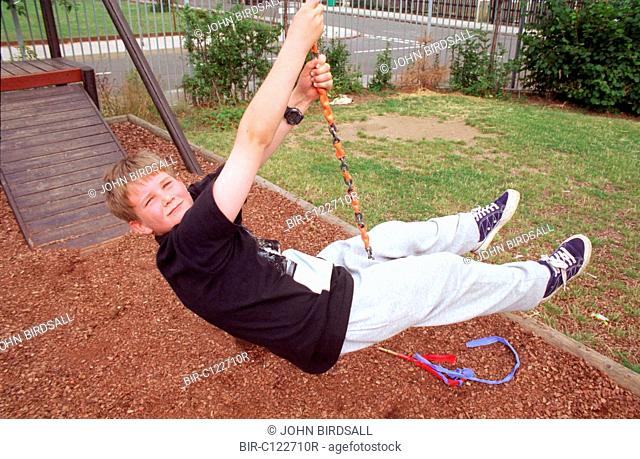 Young boy playing on rope swing in adventure playground