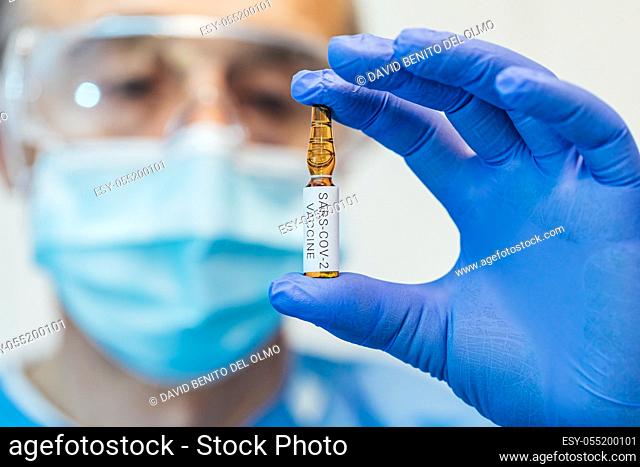 Doctor's and biologist hand with blue glove holding container with COVID-19 vaccine