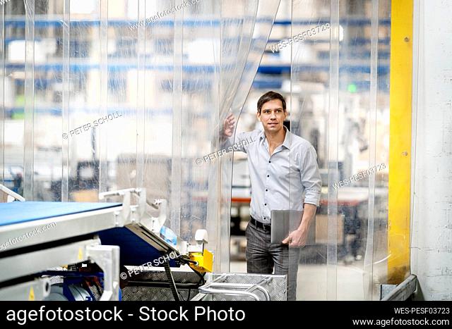 Businessman with laptop opening plastic curtain in factory