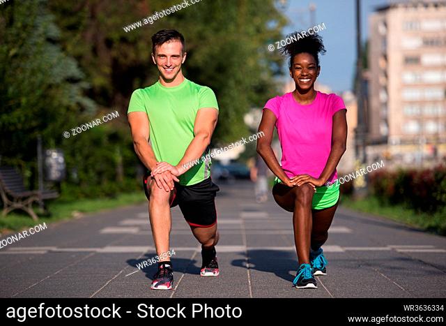 Young multiethnic jogging couple warming up and stretching before morning running in the city