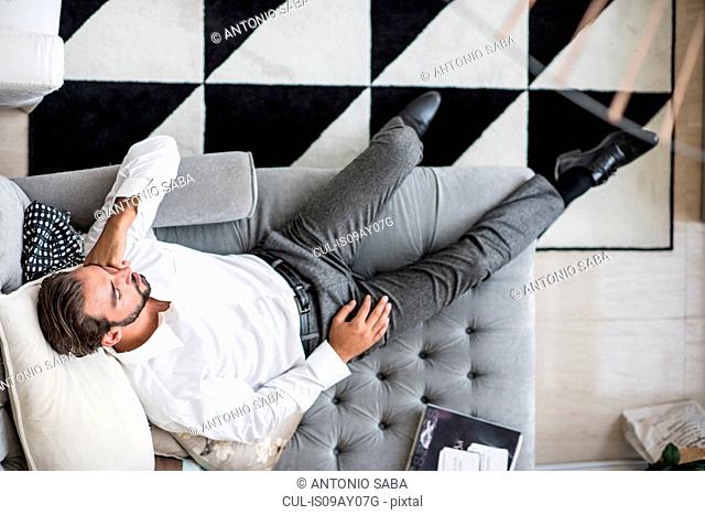 Overhead view of young businessman reclining asleep on hotel room chaise longue, Dubai, United Arab Emirates