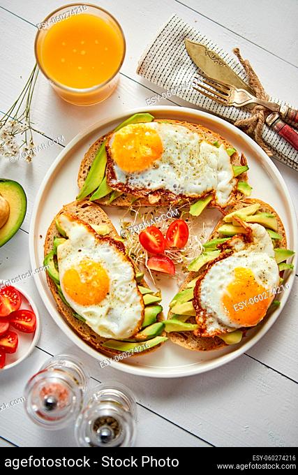 Delicious healthy breakfast with sliced avocado sandwiches with fried egg on top of bread. With orange juice, cherry tomatoes, radish sprouts, salt and peper