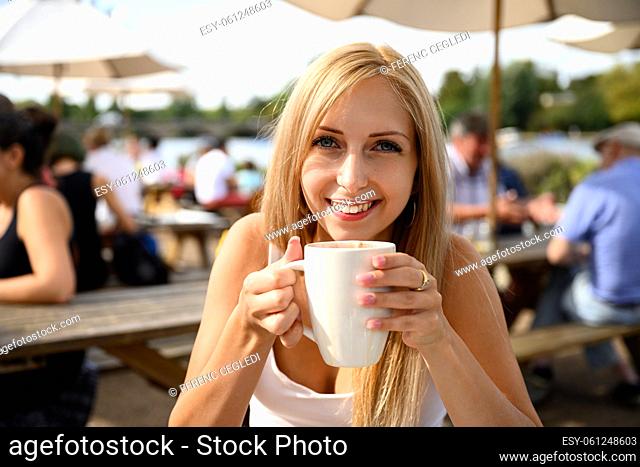 Portrait of young pretty woman in a street café with a cup of coffee latte in her hand and the London wind blowing into her hair in the United Kingdom