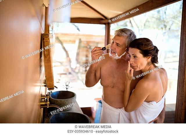 Couple standing with arm around while shaving in cottage