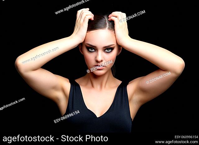Beauty portrait of young woman with hand on head on black background. Brunette girl with evening female makeup and black dess